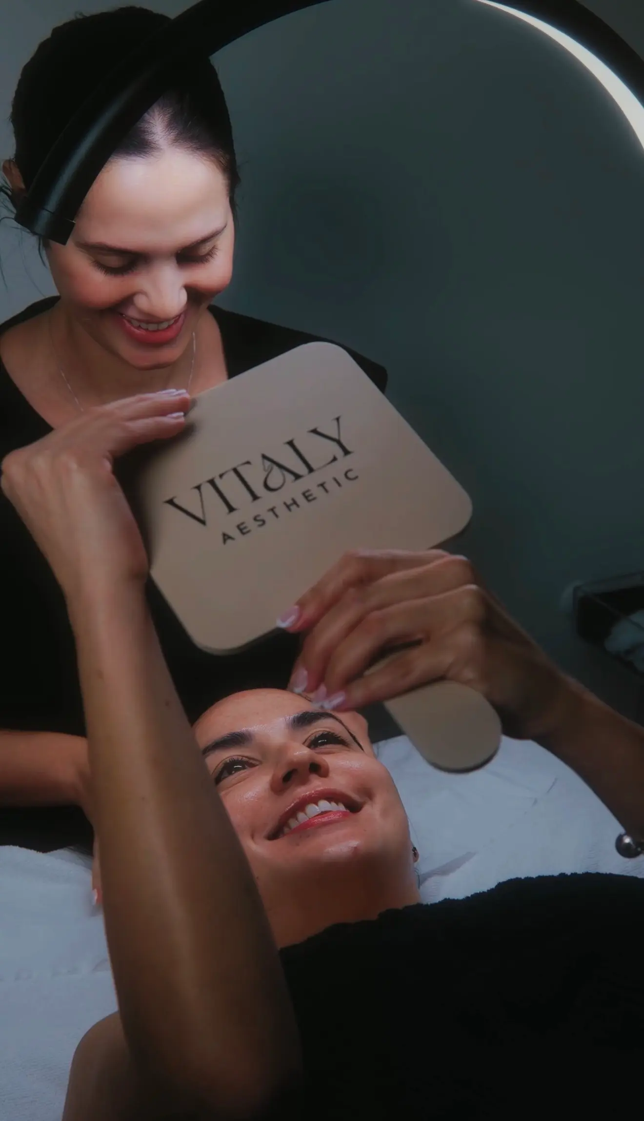 Vitaly skincare professional and a smiling client holding a Vitaly Aesthetic mirror